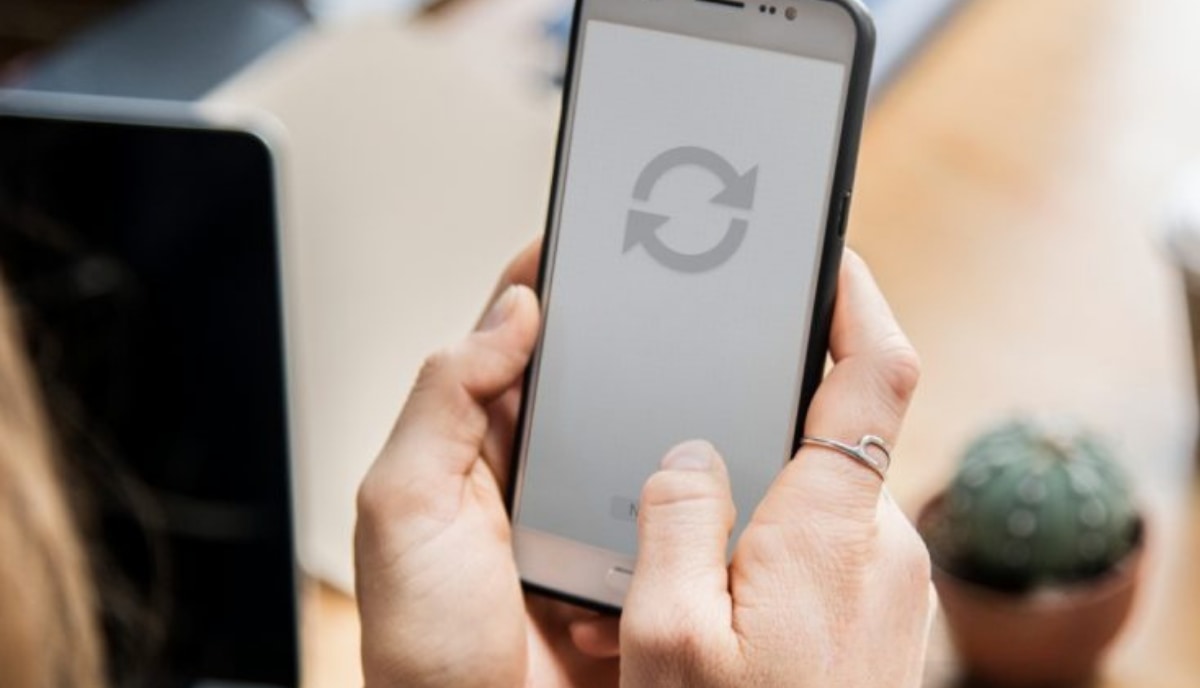 Deux mains tenant un smartphone dont l’écran affiche le symbole d’une mise à jour en cours.
