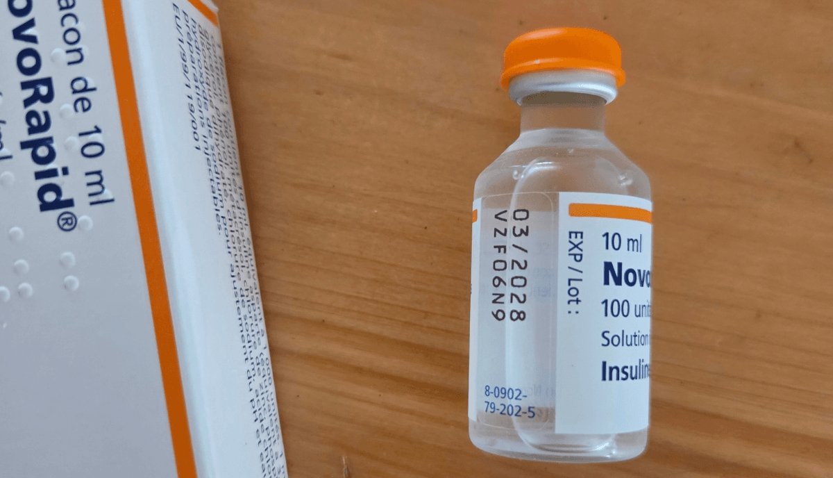 Flacon de NovoRapid 100 unités/ml de 10 ml et sa boîte, posés sur une table en bois.